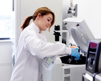 Woman in white lab coat using a machine in a lab
